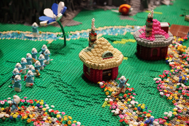 Ein Lego-Modell einer Kleinstadt mit bunten Blumen, Häusern, Pflanzen und Spielzeugen, vor einem leicht unscharfen Hintergrund.
