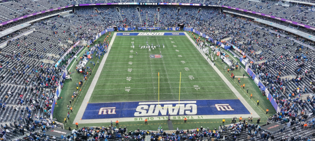Ein voller Fußballstadion mit Spielern auf dem Feld, Torpfosten und Texttafeln, von oben betrachtet mit Reihen leerer Sitze.