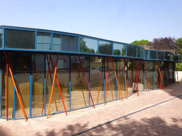 Ein modernes Schulgebäude mit zahlreichen Fenstern, einem vorderen Baumgang und einem klaren blauen Himmel darüber.