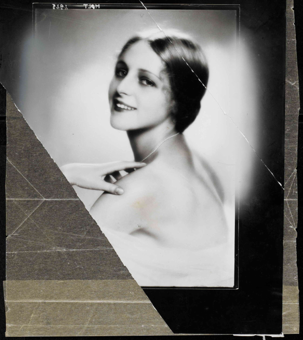 Schwarzes und weißes Porträt einer Frau in einem Kleid im Stil der 1920er Jahre mit ihrem Haar zu einem ordentlichen Knoten frisiert, die warm in die Kamera lächelt.