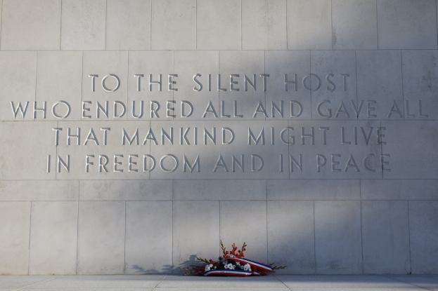 Eine Gedenktafel mit einer Inschrift, die stille Gastgeber ehrt, umgeben von einem Blumenstrauß.