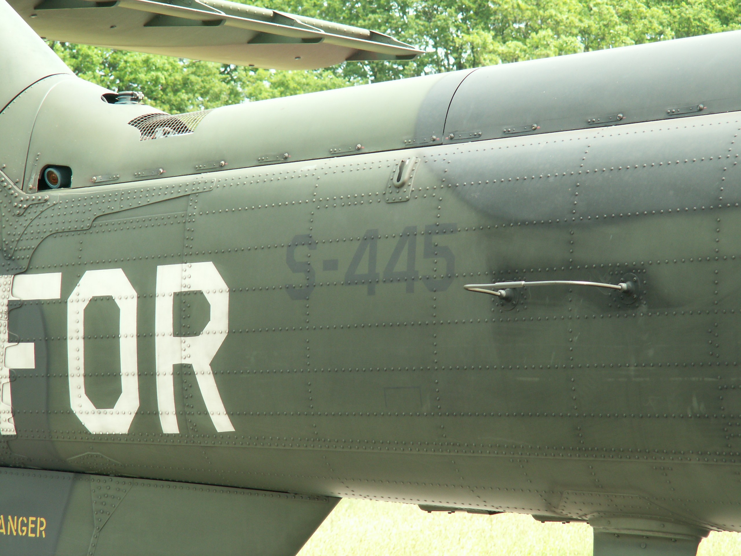Nahaufnahme eines Militärhelikopters mit dem Wort "FOR" auf der Seite, vor einem Waldhintergrund.