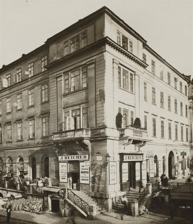 Das J Reicher Hotel in Berlin, ein altes Gebäude mit Fenstern, Treppen mit Geländern und Töpfen mit Pflanzen, mit ein paar Menschen und einem sichtbaren Himmel im Hintergrund.