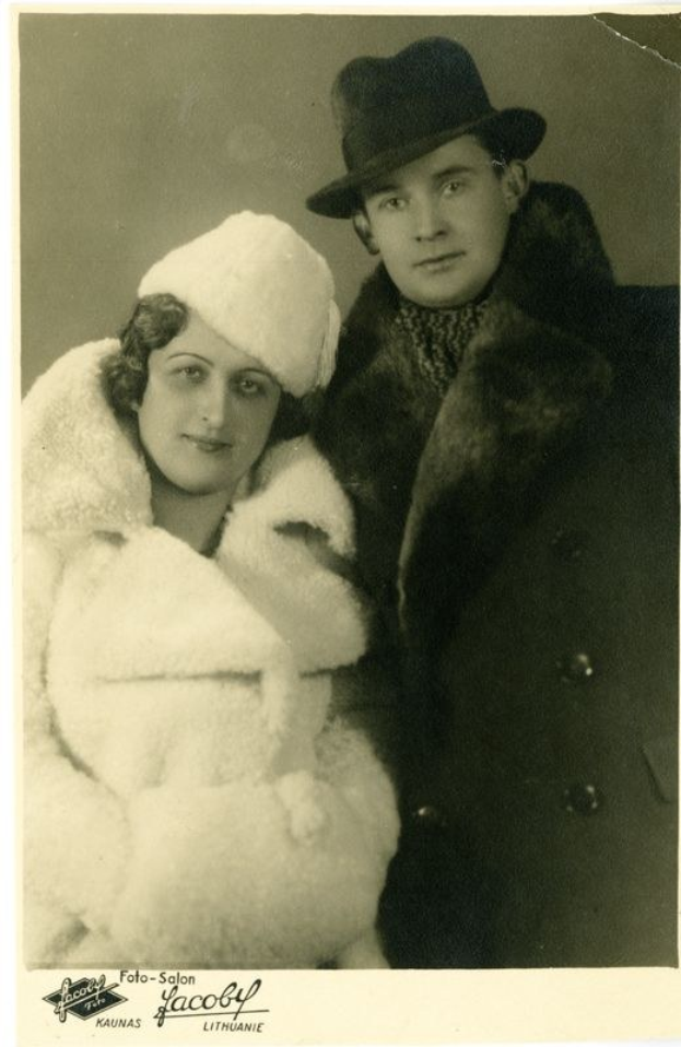 Schwarzes und weißes Foto eines Mannes in einem Pelzmantel und Hut mit einer Frau in einem Pelzmantel und Hut, die lächelt, mit Text unten.