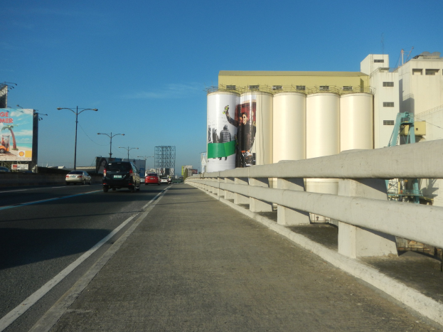 Autobahn mit fahrenden Autos, Seitenplanke, Laternenpfählen, entfernter großes Gebäude und wolkenlosem Himmel.