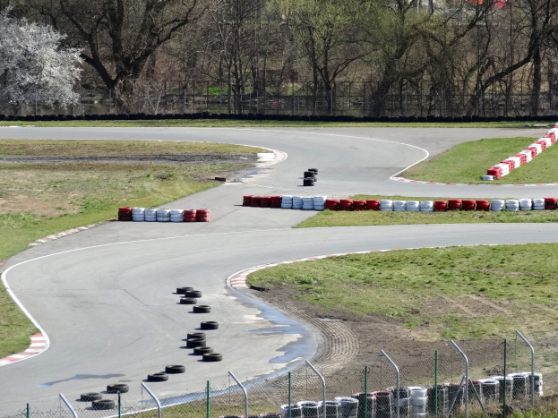 Rennstrecke mit zahlreichen Reifen darauf, umgeben von Gras und Maschendrahtzaun, mit Bäumen im Hintergrund.